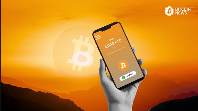 A grayscale hand holds a smartphone against an orange sunset backdrop featuring a large Bitcoin logo, with the screen displaying a transaction confirmation of "Send 1,000 BTC to" alongside a green checkmark. The "Bitcoin News" logo appears in the upper right corner, visually reinforcing the post about 6,427.59 dormant BTC ($507M) being moved in August at a daily rate of 214 BTC, 5.3 times July's volume.