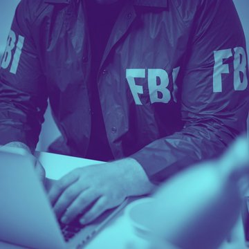 An individual wearing a jacket with "FBI" lettering works on a laptop, illustrating the federal law enforcement investigation into a $245 million cryptocurrency theft and laundering scheme led by a 22-year-old Singaporean man.