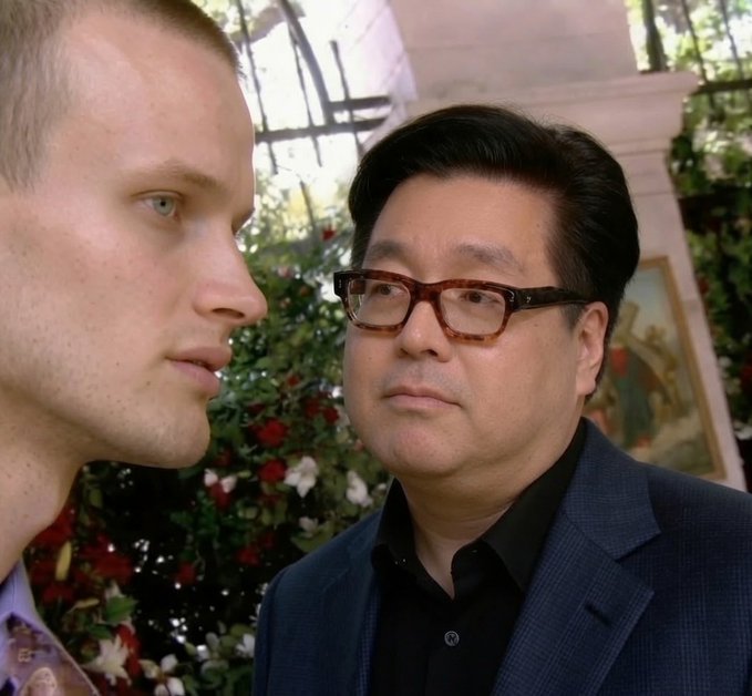 A man wearing a dark blue suit jacket stands next to another man, looking away from him while both of them look at something off-camera. In addition to these two men, there are other people present in the background who appear to be looking over their shoulders or focusing on something outside the frame of the image. The post features the CEO of a company whose name is visible but not what he is discussing with anyone in the photo. Furthermore, it appears that he has dumped 50% of his ethereum portfolio.