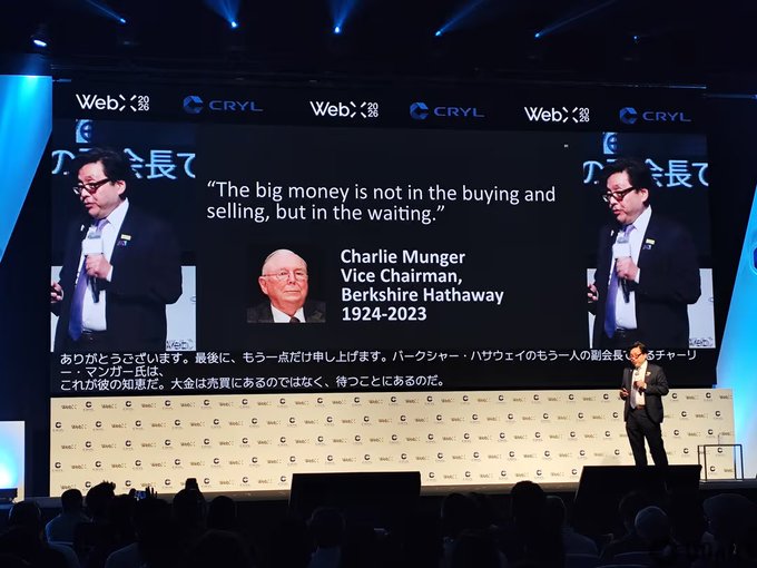 A presenter speaks at WebX 2026 alongside a slide featuring a Charlie Munger quote: "The big money is not in the buying and selling, but in the waiting," illustrating Tom Lee's on-stage argument that Ethereum is positioned as the antidote to a "wealth horror valley," echoing Munger's patience-driven investment philosophy.