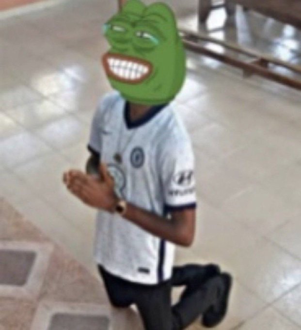 A young person wearing a white sports jersey with Hyundai and other logos kneels on a tiled floor, their face obscured by a green Pepe the Frog meme mask.