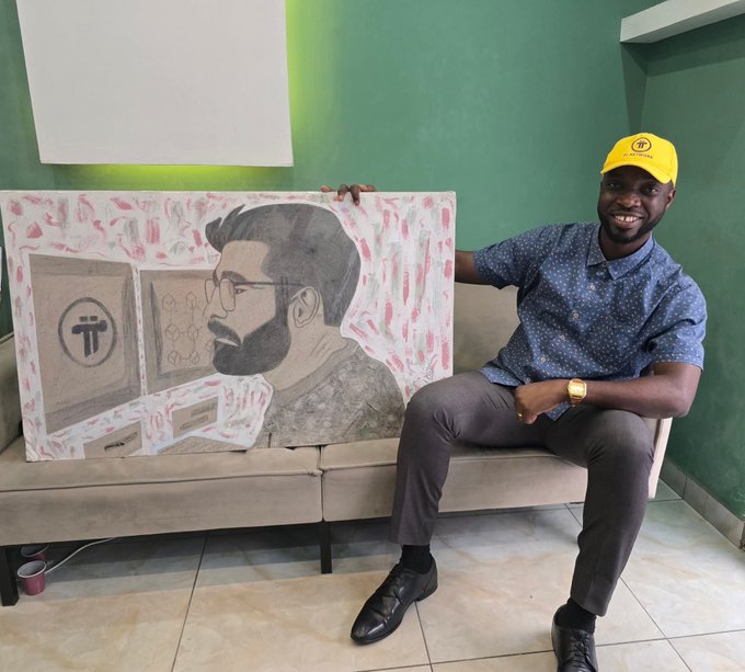 A smiling young man wearing a yellow Pi Network cap sits on a couch beside a hand-drawn portrait of a bearded man, with Pi Network logos visible in the artwork, visually celebrating the growth and involvement of the African Pi Network community.