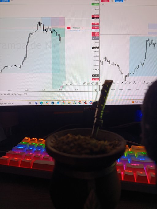 A trader's desk setup featuring a monitor displaying a NQ (Nasdaq) trading chart with what appears to be Spanish text, alongside a colorful RGB mechanical keyboard and a traditional gourd mate cup with a metal straw in the foreground.
