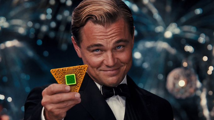 An AI-generated or edited image of Leonardo DiCaprio in a tuxedo and bow tie, smiling while holding up a golden triangular microchip with a green center, resembling a scene from The Great Gatsby.
