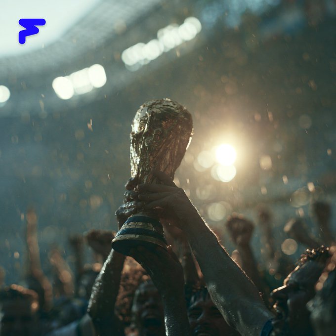 A triumphant hand lifts the FIFA World Cup trophy aloft in a stadium illuminated by a brilliant spotlight, with a silhouetted crowd cheering in the background. The golden cup, gleaming against the hazy, bokeh-lit arena, symbolizes the global event that Avalanche's blockchain technology is helping protect from ticket scalping.