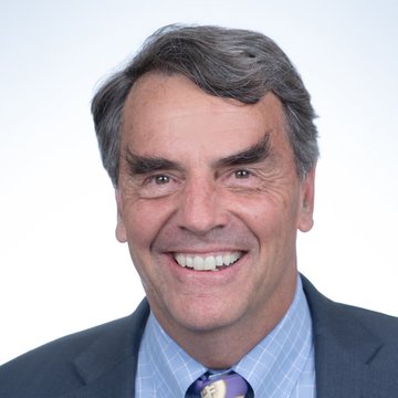 A headshot of billionaire Tim Draper smiling warmly, dressed in a dark suit with a light blue checkered shirt and purple patterned tie, accompanying news that he denied moving his Bitcoin to Coinbase while maintaining his bullish $250K price prediction.