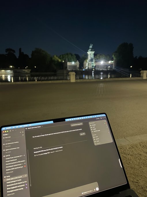 A nighttime photo showing a laptop screen with chat messages in the foreground, with an illuminated monument and bridge visible in the background across a plaza.