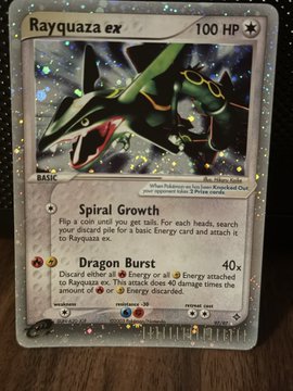 A holographic Rayquaza ex Pokémon card (100 HP) featuring moves "Spiral Growth" and "Dragon Burst" (40x damage), shown as the item for sale with a firm price of $500 shipped, listed as NFT (not for trade) on a wooden surface.