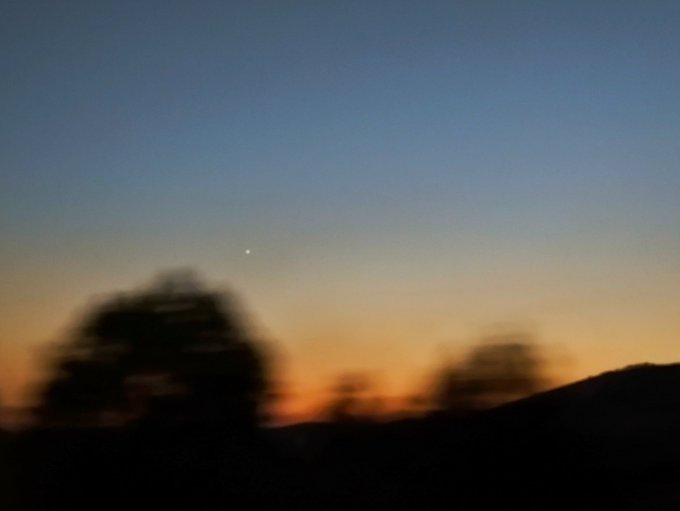 A blurry sunset scene with silhouetted trees and hills, and a small bright point (possibly a planet or star) visible in the twilight sky.