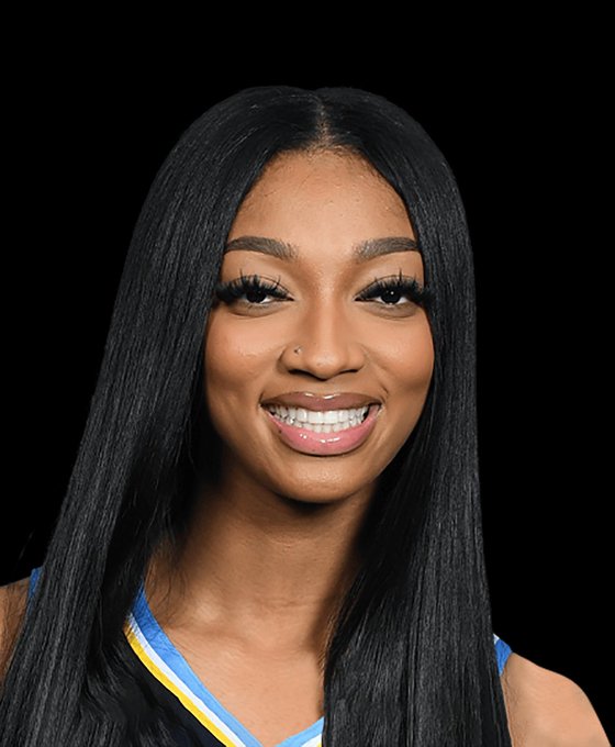 A studio portrait of a smiling young woman with long straight black hair, wearing a blue and yellow jersey, set against a solid black background.