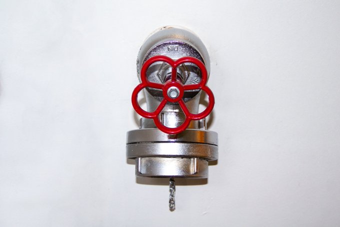 The image features a red valve with a silver handle, which appears to be part of an industrial machine or equipment. The valve has a unique design that makes it stand out against the white background. The post discussing this valve seems to be about the importance of the valve in the context of Tezos Tuesday and the @drylinemix community.