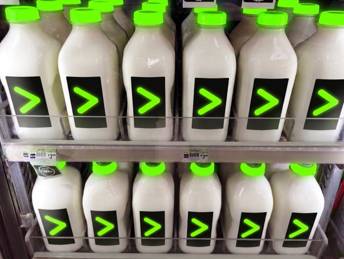 Store shelves are stocked with rows of white bottles featuring bright green caps and black labels with green chevron arrows.