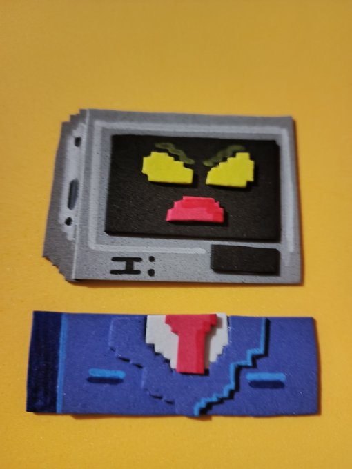 A 3D-printed object resembling a floppy disk with a face on the screen, placed above a blue object resembling a cassette tape with a pink tie, set against a yellow background.