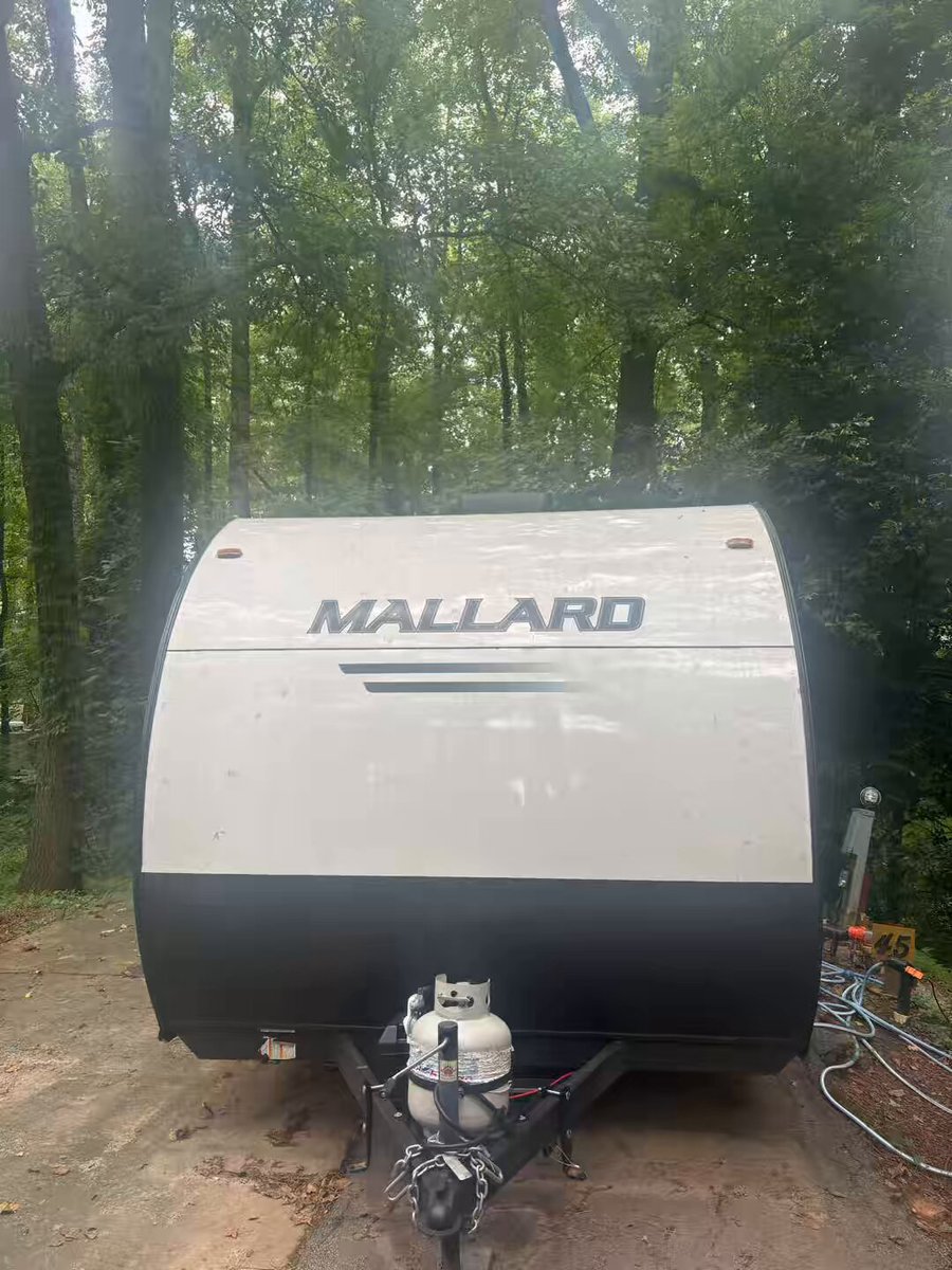 The image features a white and black recreational vehicle (RV) parked next to trees in a wooded area. The RV has a "Mallard" logo on its side, indicating that it's likely a model from the company. The post about Bitcoin Maxi living in an RV is related to the RV because it suggests that the person who wrote the post lives in or uses the RV as their primary residence and has chosen to live off the grid by using Bitcoin for financial transactions. This lifestyle choice allows them to minimize their expenses, such as rent payments, and maximize their savings while enjoying a simpler way of living.