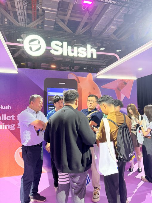 A group of attendees gathers at the Slush booth during the Singapore TOKEN2049 conference, where the SUI ecosystem showcase spans an entire floor featuring its various projects, including the official Slush Wallet seen in use on the adjacent vending machine for purchasing drinks with SUI.