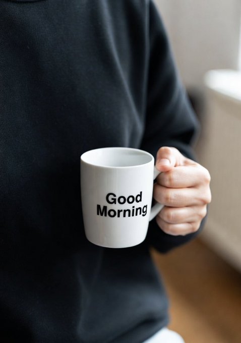 A person in a black sweatshirt holds a white mug with "Good Morning" printed on it.