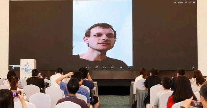An audience watches a large screen displaying a man's face during what appears to be an Ethereum conference presentation.