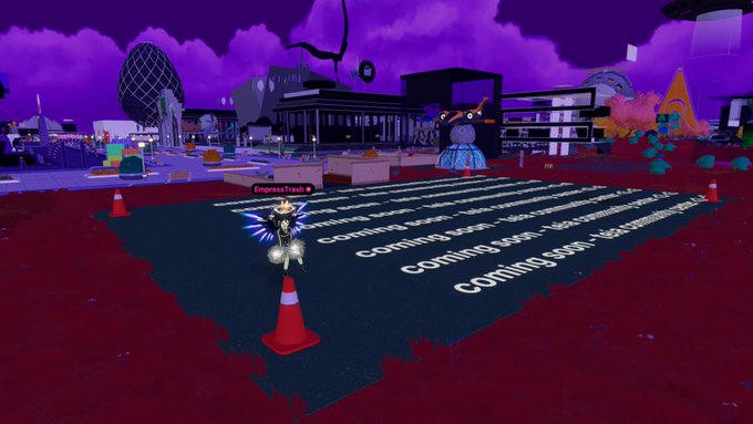 The image features a large, colorful cityscape with buildings of various sizes and shapes, including a prominent skyscraper. The sky above is a deep purple color, creating an interesting contrast against the urban backdrop. In the foreground, there are orange traffic cones placed on a red surface, possibly indicating construction or maintenance work in progress. A person can be seen standing near these cones, likely overseeing the project.