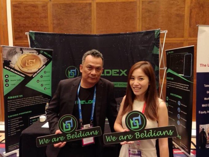 Two people, a man and a woman, standing at a 'BELDEX' promotional booth, both holding signs that read 'We are Beldians' with the Beldex logo.