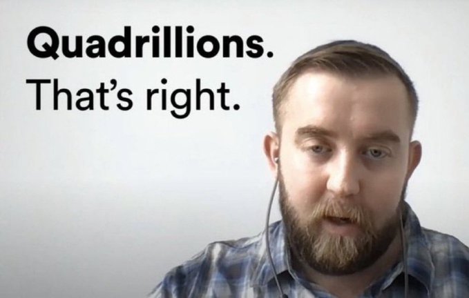 A bearded man in a blue plaid shirt wearing earphones speaks to the camera with the on-screen text 'Quadrillions. That's right.'