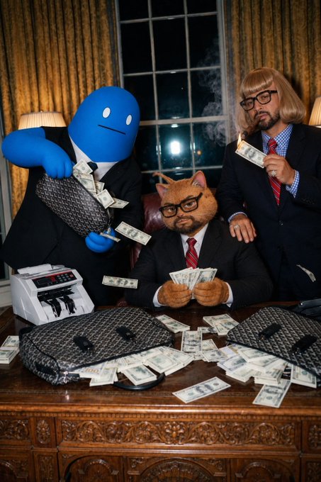 A whimsical scene featuring three costumed figures: a blue humanoid, a cat-headed person, and a blonde-wigged man, all dressed in business attire and surrounded by scattered U.S. dollar bills on an ornate wooden desk.