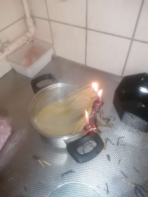 A pot of spaghetti is cooking on a stove, with the dry pasta ends on the right side accidentally catching fire and burning.
