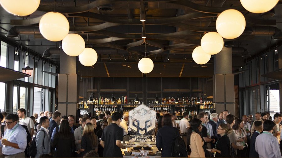 A crowded bar scene at the RWA Summit, where attendees networking in business attire gather around a central illuminated RWA logo, reflecting the event's role as a hub for those building the future of real-world asset tokenization.