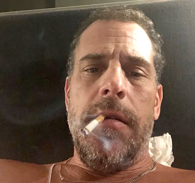 A man with a beard smoking a cigarette, looking directly at the camera.