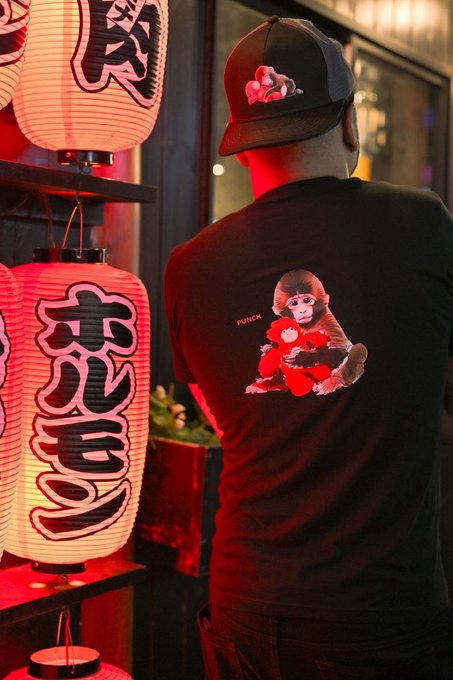 A person from behind wearing a black t-shirt and cap with monkey designs, standing near glowing red Japanese lanterns.