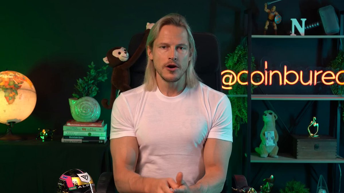 The image features a man wearing a white t-shirt, sitting behind a desk with a globe next to him. The man appears to be giving a speech or presentation about coinburec.