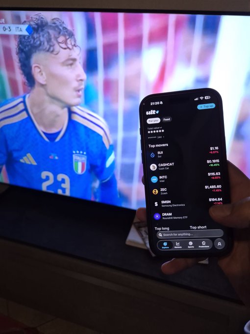 A hand holds a smartphone displaying the Self cryptocurrency app with trending tokens and their prices, set against a TV showing a soccer match featuring a player in an Italy jersey (#23) with the score '0-3' visible.