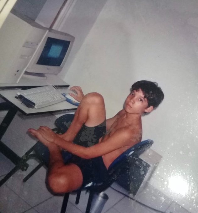 A humorous old photograph showing a young man sitting in a chair with his legs bent backwards while using an old desktop computer setup.