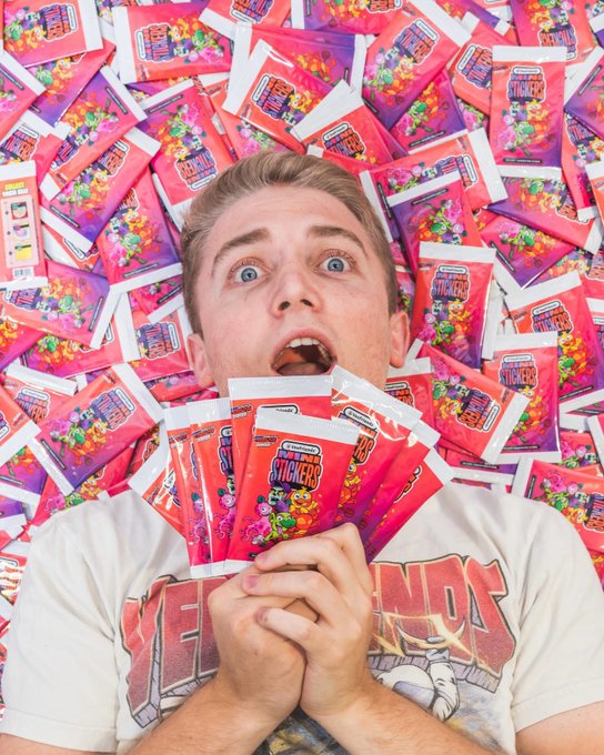 A man with a surprised expression holding multiple packs of SweeTarts Snickers candy, surrounded by a pile of identical candy bags.
