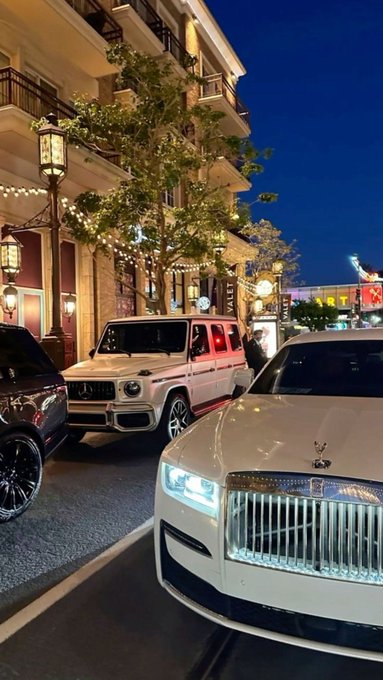 urns of a white Mercedes-Benz Sprinter, a black SUV, and a white Rolls Royce are parked on a city street at night.