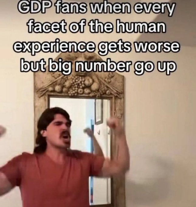 This image features a man standing next to a mirror with his arms raised, making a funny face. The text displayed below him reads "GDP fans when every facade of the human experience gets worse but big number go up", which seems to be related to the topic or theme of the image, possibly referring to something about the stock market or economy.