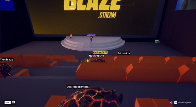 A first-person view of a virtual 3D theater with orange seats, where several avatar characters are gathered before a stage displaying the text "BLAZE STREAM."