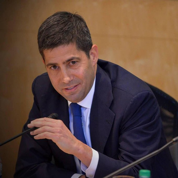The image shows a man wearing a suit and tie sitting at a table with his hand on his chin, suggesting deep thought or contemplation. The background features a yellow wall, which contrasts with the man's dark suit. The caption reads "The U.S. isn't banning crypto, it’s regulating it. mandatory KYC for stablecoin issuers is coming. While this raises concerns about privacy, it could accelerate institutional adoption". This image seems to be related to a discussion or presentation on the regulation of cryptocurrencies and their impact on financial systems in the United States.