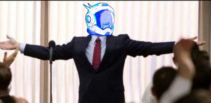 A man in a dark pinstripe suit and red tie standing at a microphone with his arms outstretched, his head digitally replaced with a blue and white robot or astronaut helmet design.