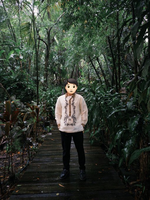 A person stands on a wooden boardwalk in a lush tropical forest, wearing a traditional Filipino Barong Tagalog shirt with intricate embroidery. The figure's face has been replaced with a Memoji, and their caption identifies them as a 28-year-old content creator from the Philippines looking to connect with others.