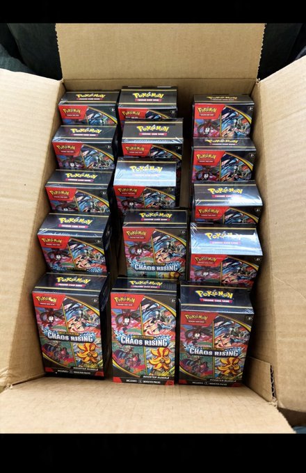An open cardboard shipping box filled with multiple sealed Pokémon Trading Card Game 'Chaos Rising' booster boxes stacked in neat rows.