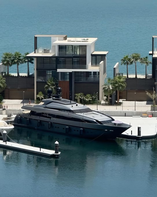 A sleek black luxury yacht is docked in front of a modern multi-story waterfront villa with palm trees, illustrating the post's humorous trade-off of selling crypto (SOL) toward a down payment on such a high-end seaside property.