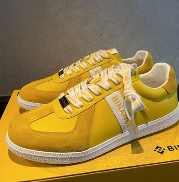 A pair of yellow Binance-branded sneakers displayed on a yellow box featuring the "BINANCE" logo and wordmark on the side strap, reflecting the post's praise for the high-quality cryptocurrency exchange merchandise that recently became available.