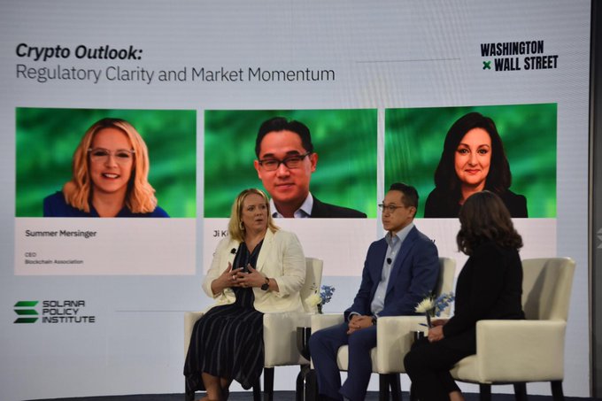 A panel discussion at a 'Washington x Wall Street' event titled 'Crypto Outlook: Regulatory Clarity and Market Momentum,' featuring three speakers on stage, including Summer Mersinger (CEO, Blockchain Association) displayed on the backdrop screens, with Solara Policy Institute branding.