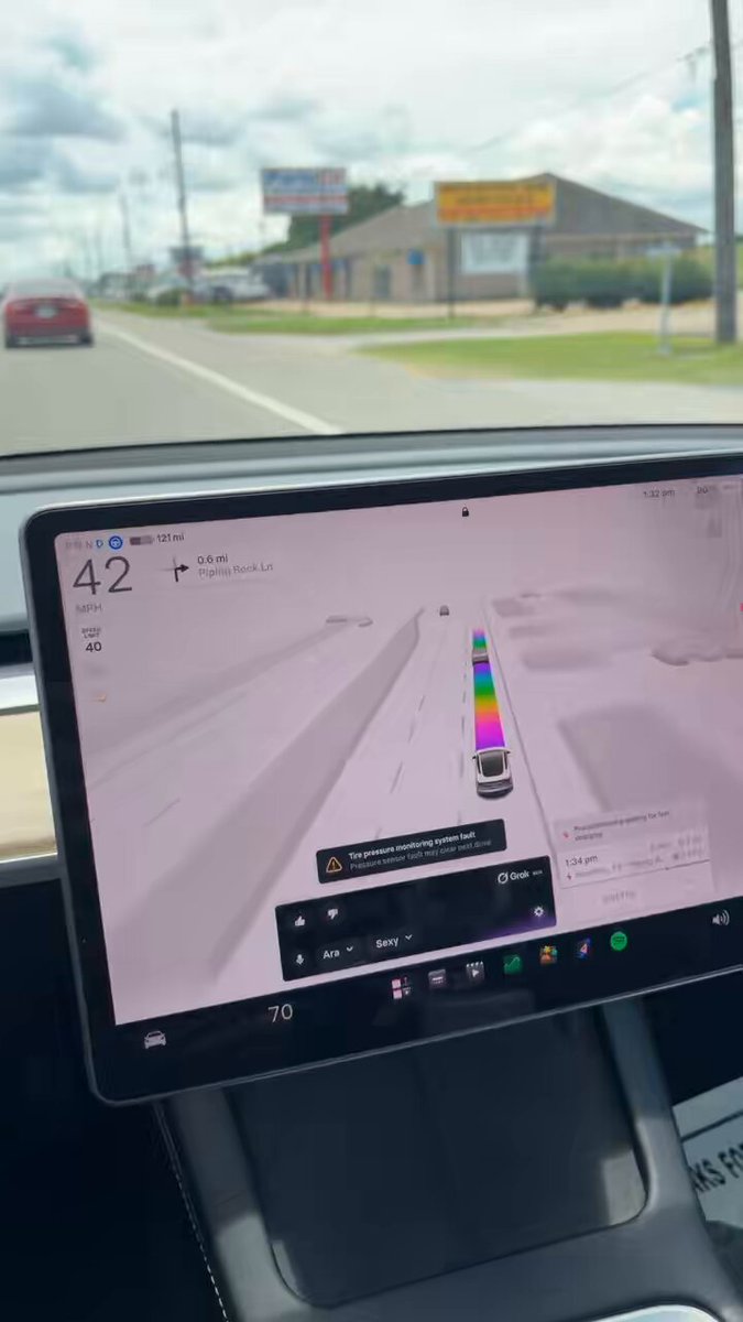 The image features a car dashboard with an electronic display showing a traffic map, likely used for navigation or real-time traffic updates by Tesla drivers. The screen displays a colorful line drawing of various vehicles, which is likely related to the concept of Ravencoin as indicated in the caption. The car's driver appears to be focused on the driving route displayed on the dashboard while the image of the "Tesla's take on Ravencoin." suggests that they might have some interest in digital currency or innovative transportation solutions.