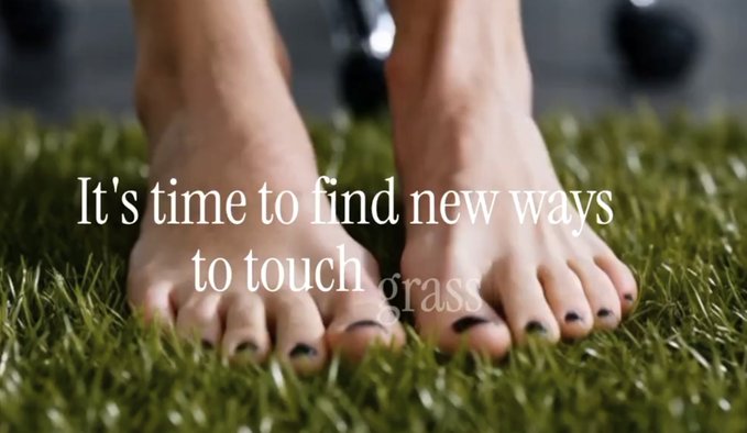 The image shows a person's feet standing on a green carpet or grass, with text that reads "It's time to find new ways to touch grass". The caption also includes an instruction for users to not use their feet as part of their index launch in any online platform.