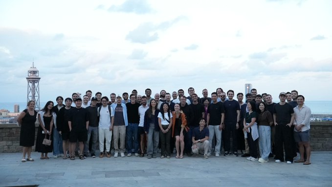 A large group photo of people posing outdoors on a rooftop with a tall tower and ocean visible in the background.