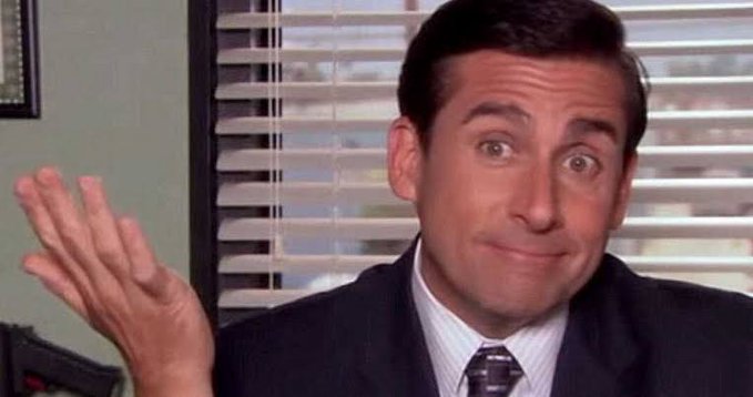 A man in a suit making a skeptical, shrugging gesture with his hand raised, known as the 'Michael Scott shrug' meme.