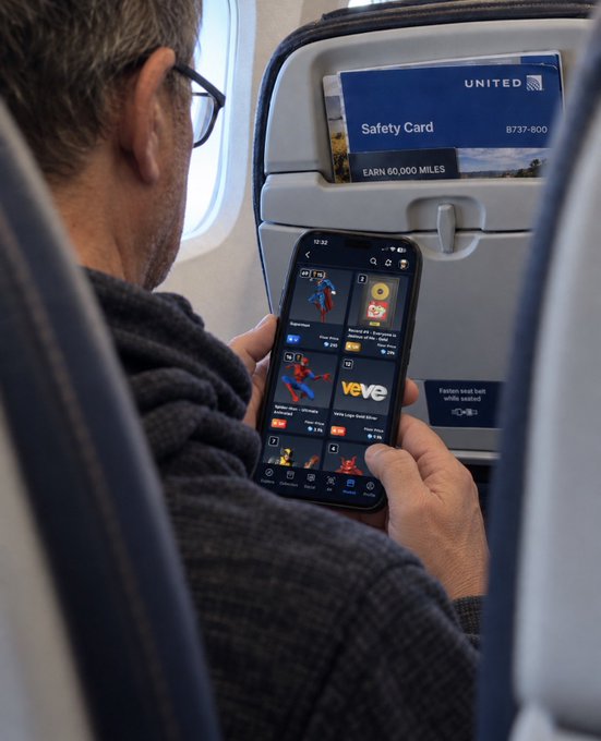 A man sitting in a United Airlines B737-800 seat browsing the VeVe app on his smartphone, with a Safety Card visible in the seatback pocket.