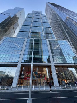 A low-angle photograph of a modern glass skyscraper with a grid-patterned facade, reflecting the surrounding city buildings.