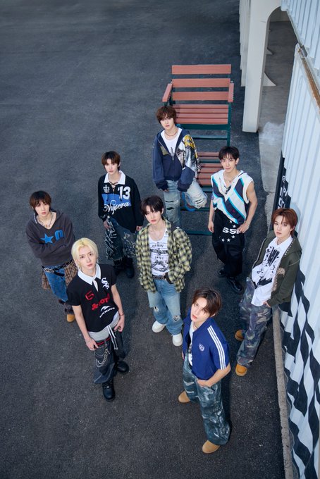 A group of nine young men in casual, Y2K-style streetwear posing on an outdoor staircase and pavement.